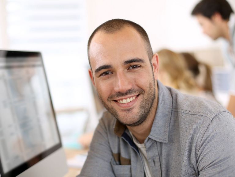 Mitarbeiter vor Computer lächelt in die Kamera