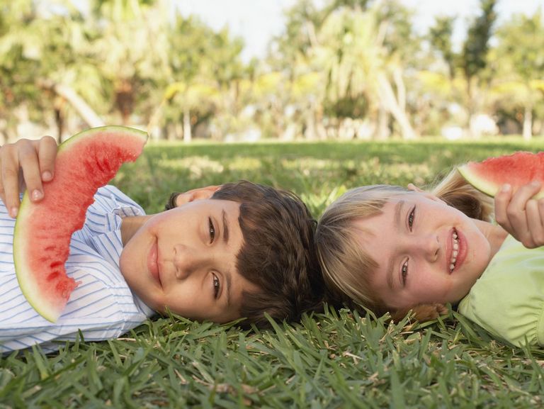 2 Kinder liegen auf der Wiese und essen Wassermelone