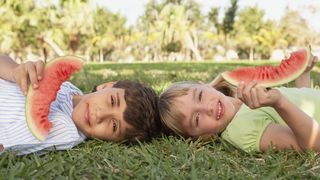 2 Kinder liegen auf der Wiese und essen Wassermelone