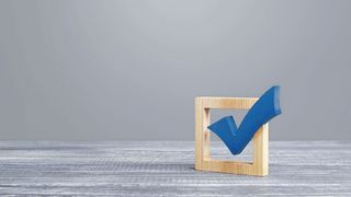 Ergebnis-Check Auf einem grauen Tisch steht ein Kästchen mit einem blauen Häkchen darin