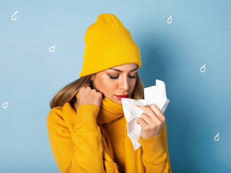 Frau mit gelbem Pullover und gelber Mütze hält ein Taschentuch vor ihre Nase