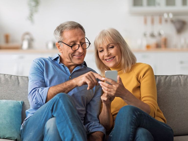 Älteres Paar sitzt auf einer Couch und nutzt gemeinsam ein Smartphone