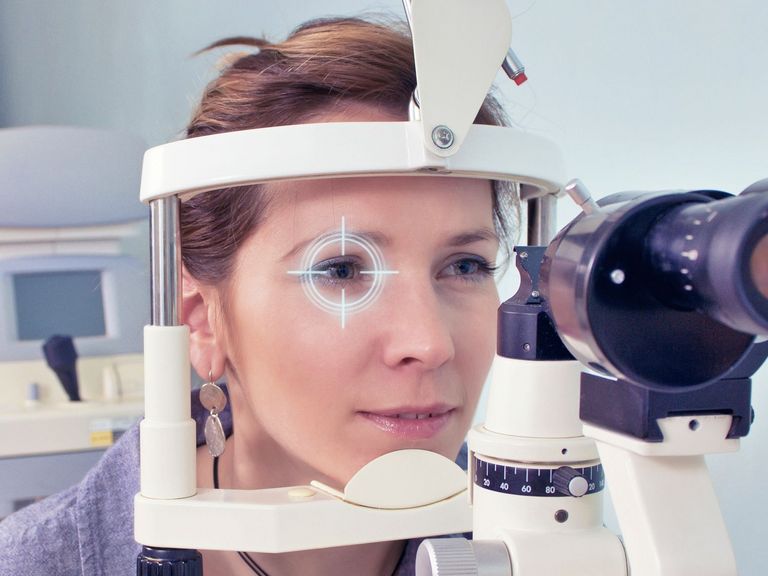 Frau schaut durch ein Messinstrument beim Augenarzt