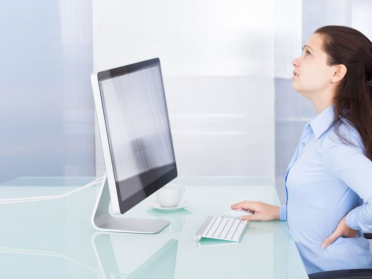 Frau am Büroarbeitsplatz hat Rückenschmerzen