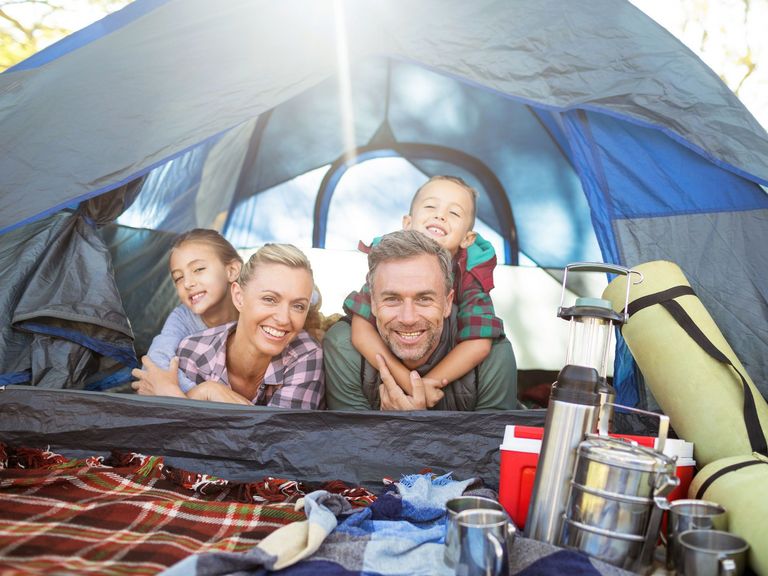 Familie liegt in einem Zelt mit allerlei Campingausrüstung und schaut gemeinsam lachend hinaus