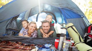 Familie liegt in einem Zelt mit allerlei Campingausrüstung und schaut gemeinsam lachend hinaus