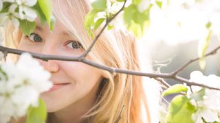 Junge Frau schaut durch die Zweige eines blühenden Baumes