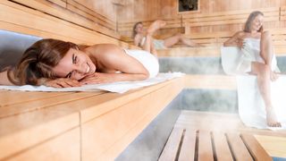 Zwei Frauen in der Sauna, eine der beiden liegt bäuchlings und lacht in die Kamera