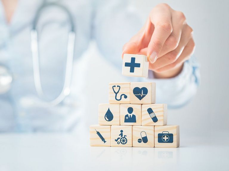 Würfelpyramide mit Symbolen aus dem Gesundheitswesen und einer Ärztin mit Stethoskop im Hintergrund