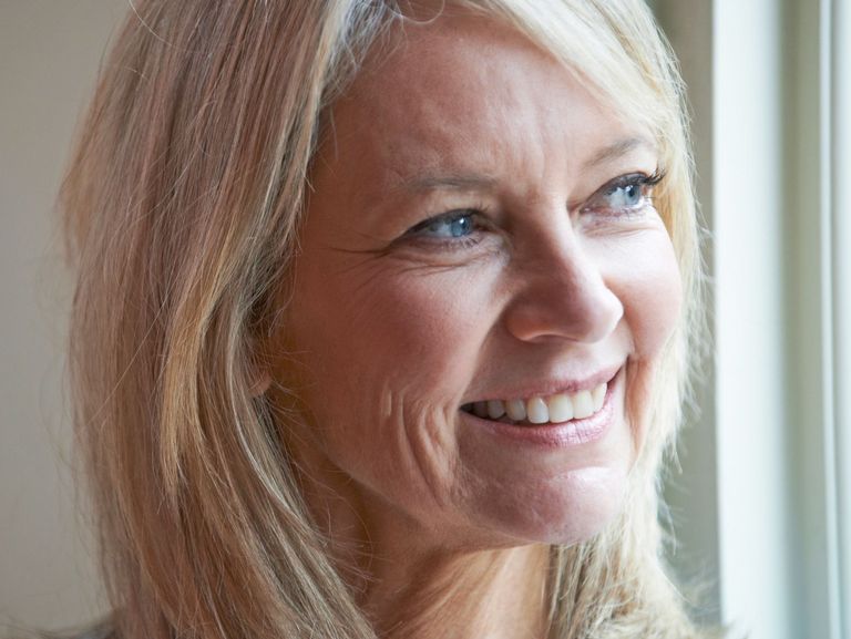 50-jährige Frau schaut lächelnd zum Fenster hinaus