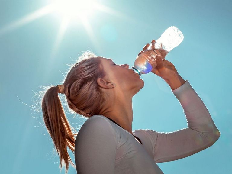 Junge Sportlerin trinkt in der Sommerhitze Wasser aus einer Flasche