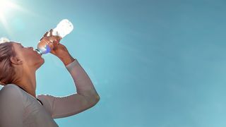 Fit in der Sommerhitze Junge Sportlerin trinkt in der Sommerhitze Wasser aus einer Flasche