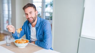 Trinken beim Essen Mann mit Bart siitzt in der Küche beim Mittagessen und auf dem Tisch steht ein Glass mit Wasser