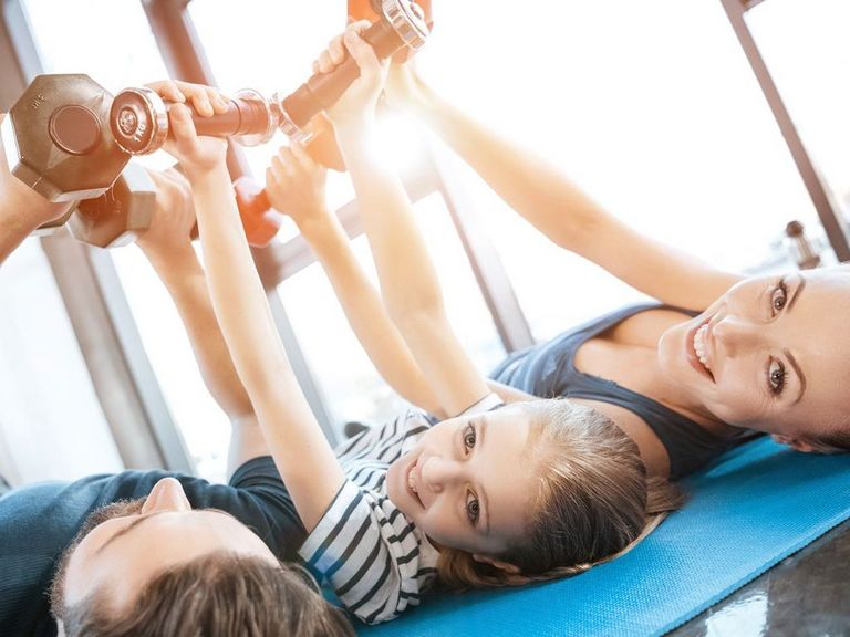 Dreiköpfige Familie liegt auf einer Turnmatte und trainiert mit Hanteln in der Luft