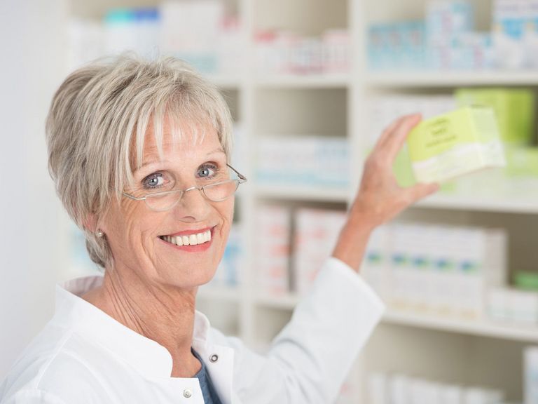 Ältere Apothekerin holt Medikamente aus dem Regal