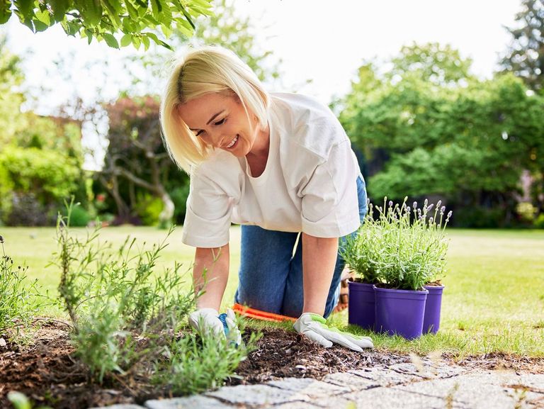 Frau kniet vor einem Beet auf dem rasen und verrichtet mit Freude Gartenarbeit