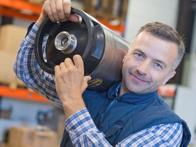 In einem Lager arbeitender Mann trägt etwas schweres auf der Schulter