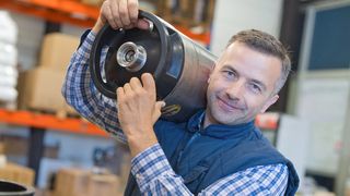 In einem Lager arbeitender Mann trägt etwas schweres auf der Schulter