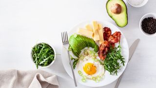 Auf einem Tisch steht ein Teller mit Lebensmitteln für die ketogene Ernährung, wie Eier, Avocado, Fleisch und Käse