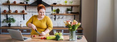 Frau bereitet unter Anleitung per Laptop Essen in einer Küche zu