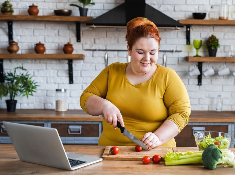 Frau bereitet unter Anleitung per Laptop Essen in einer Küche zu
