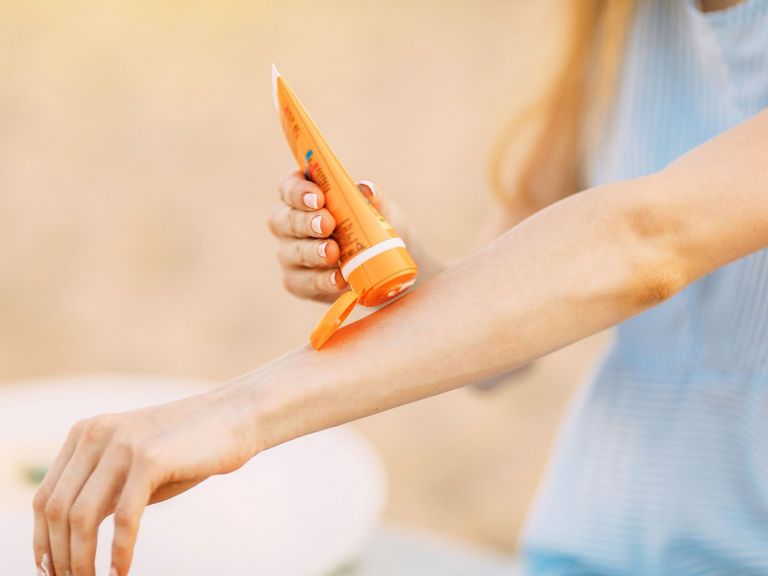 Frau macht aus einer Tube etwas Sonnenschutzcreme auf ihren ausgestreckten Unterarm