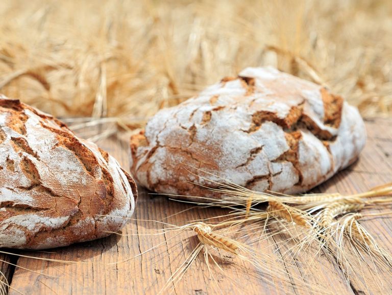Zwei Brotlaibe und Getreideähren auf einem Holztisch