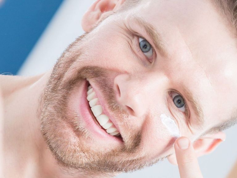 Mann schaut lachend in einen Spiegel und cremt sich das Gesicht ein