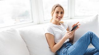 Frau mit einem Smartphone in der Hand sitzt auf dem Sofa