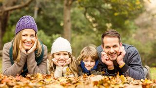 4-köpfige Familie in warmer Kleidung liegt im Herbstlaub