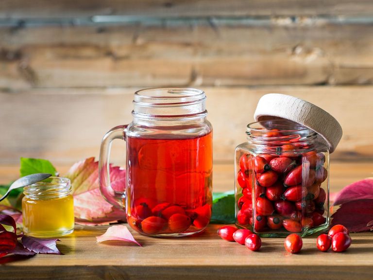 Hagebuttentee und frische Hagebutten in einem Glas stehen auf einem Holztisch