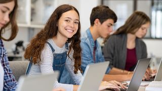 Schüler sitzen in der Schule am Laptop und ein Mädchen lächelt in die Kamera