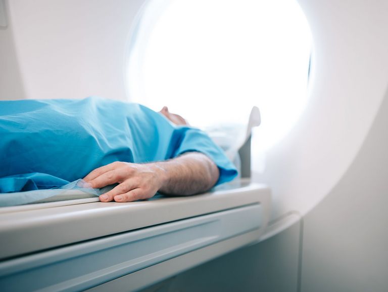 Mann in blauem Kittel liegt auf einer MRT-Liege