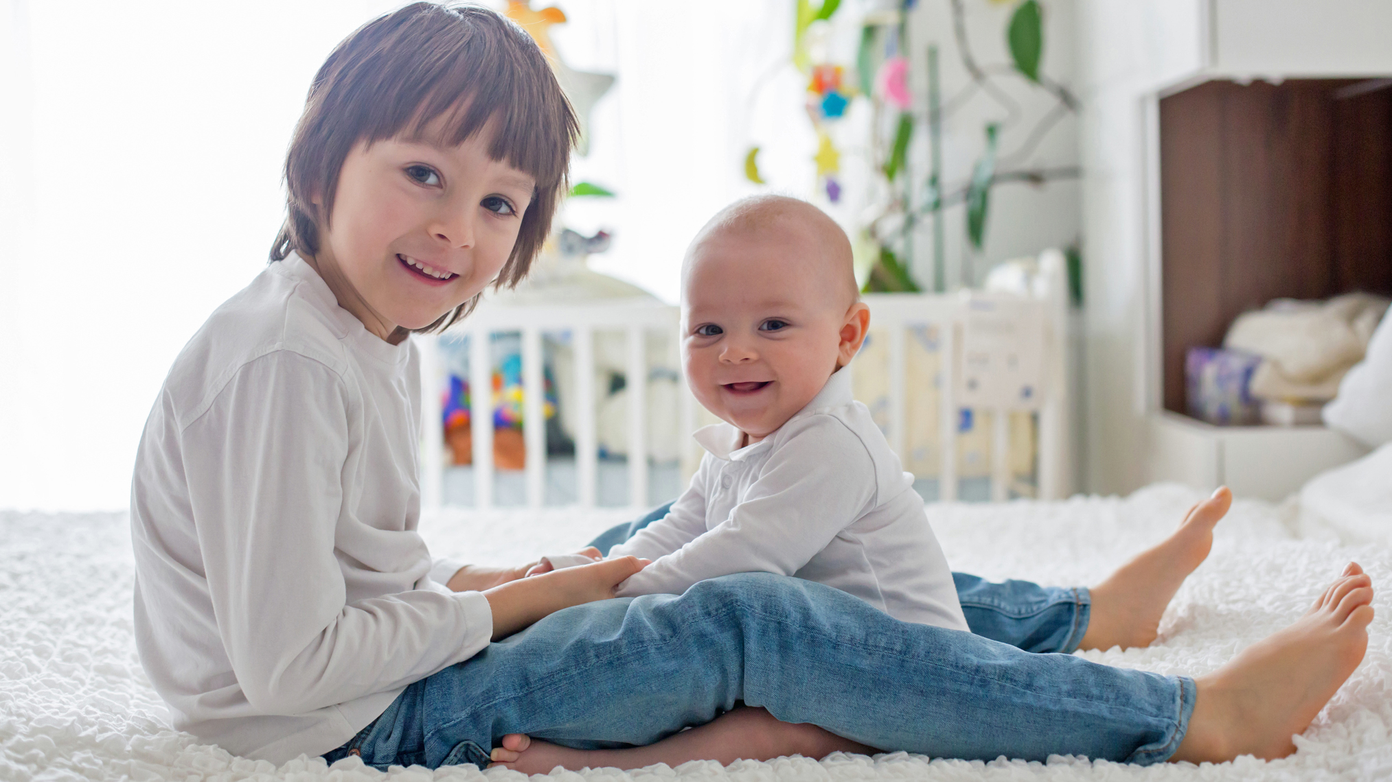 Schulkind und Baby sitzen auf einem Bett