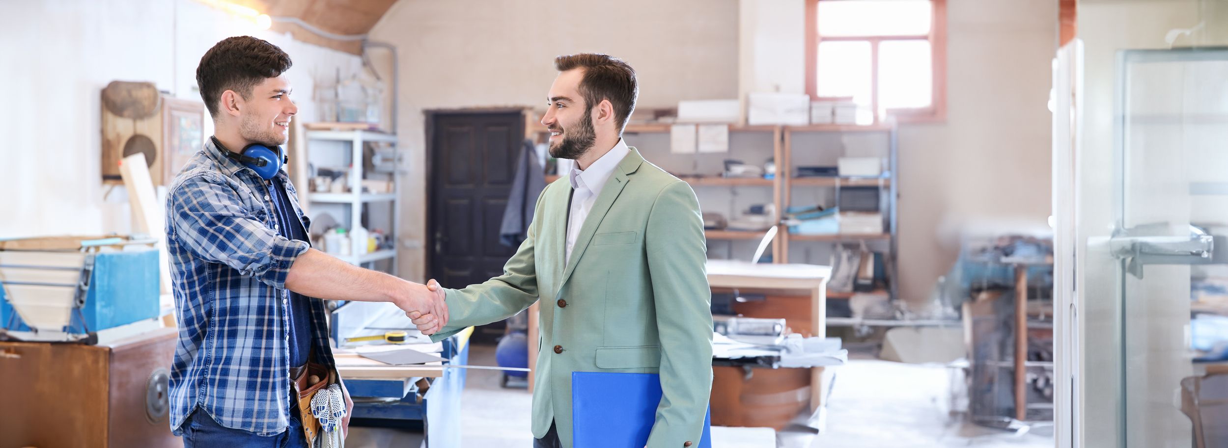 Versichert als Auszubildender Handschlag vom Arbeitgeber mit seinem Azubi in einer Werkstatt