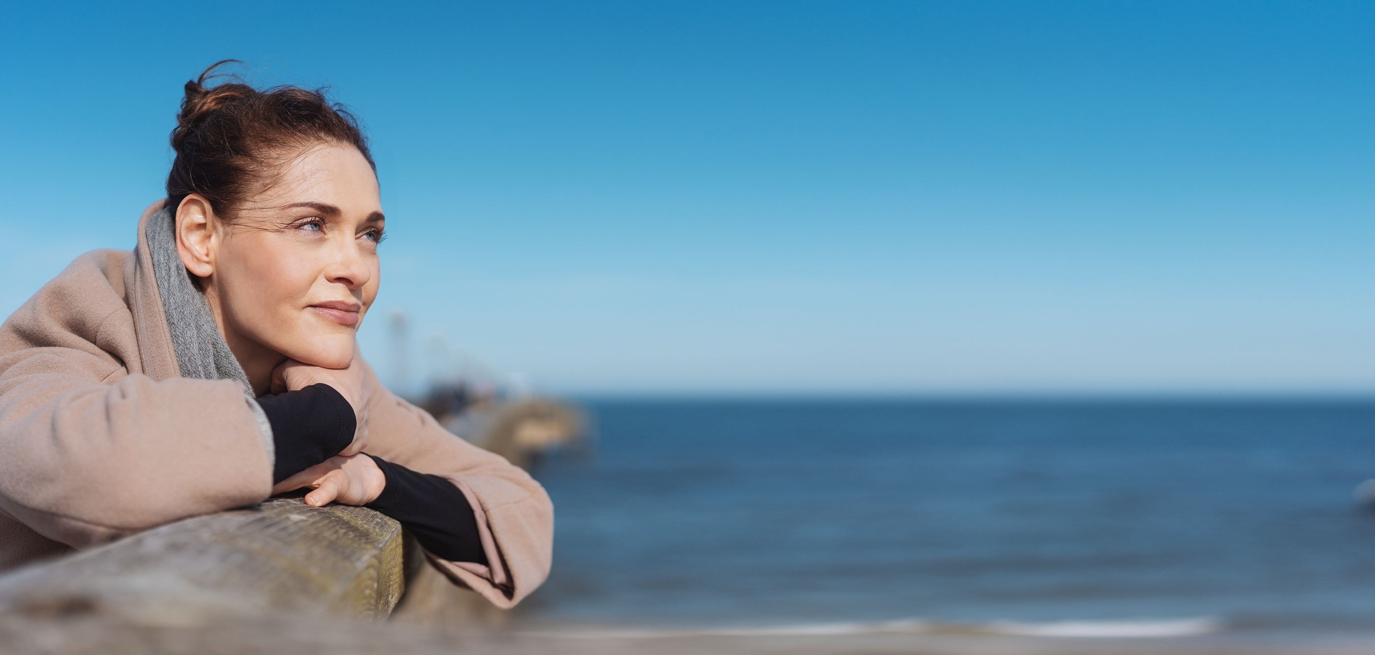 Frau im Portrait auf einer Seebrücke an einem Strand bei Sonnenschein