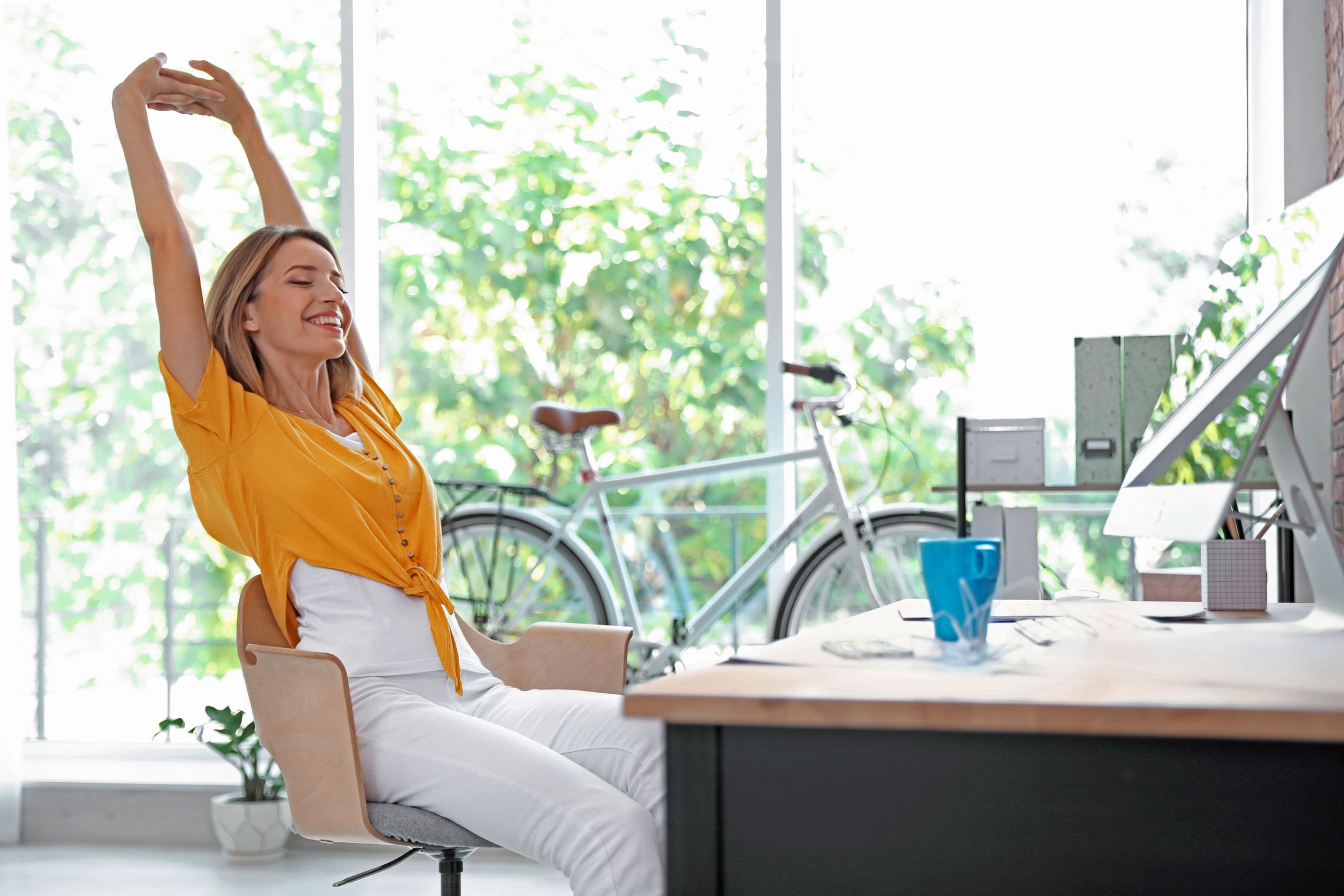 Frau sitzt im Büro an einem Schreibtisch und streckt ihr Arme nach oben