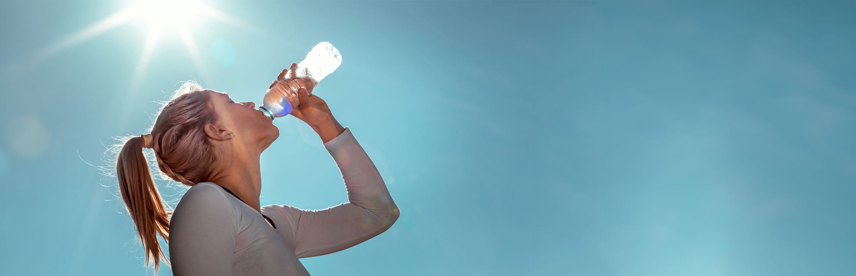 Junge Sportlerin trinkt in der Sommerhitze Wasser aus einer Flasche