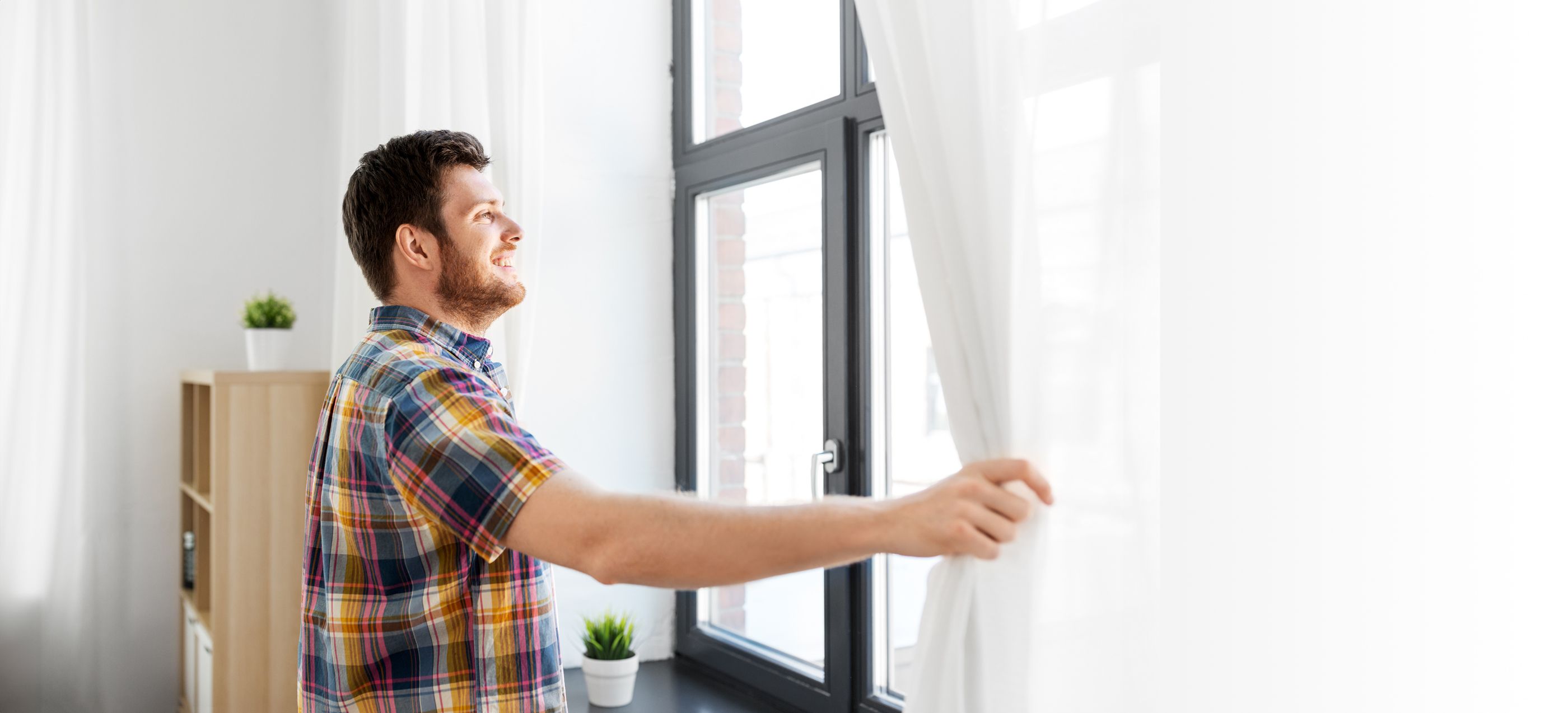 Mann möchte ein Fenster öffnen und schiebt dafür die Gardine beiseite