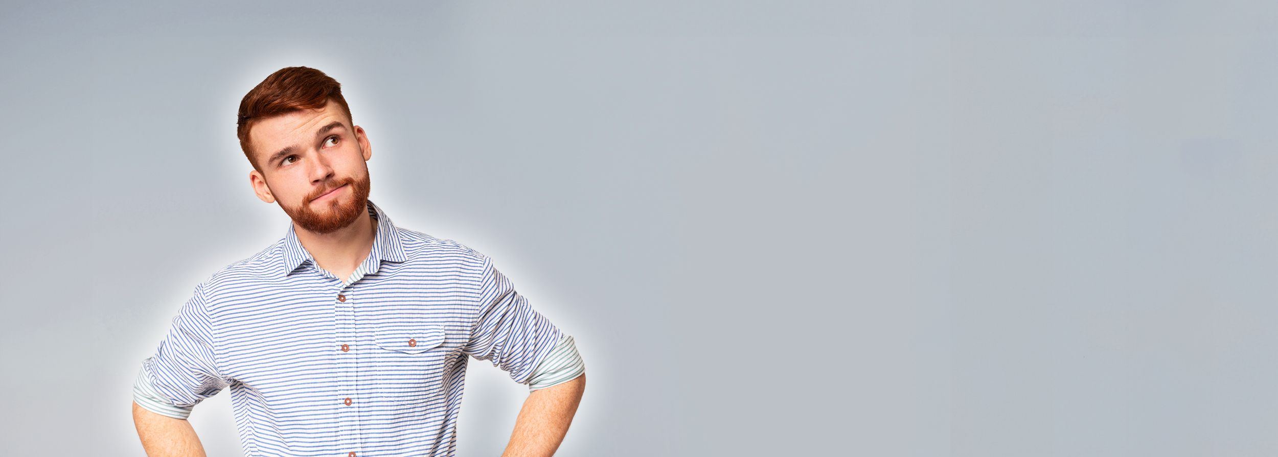 Junger Mann mit Bart schaut fragend und überlegend nach oben rechts