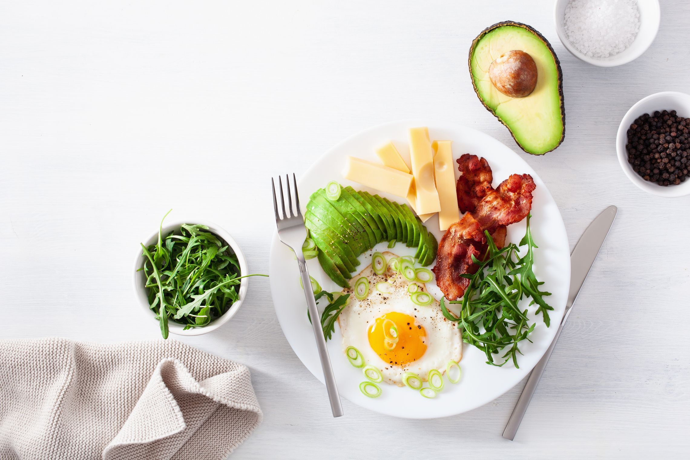 Auf einem Tisch steht ein Teller mit Lebensmitteln für die ketogene Ernährung, wie Eier, Avocado, Fleisch und Käse