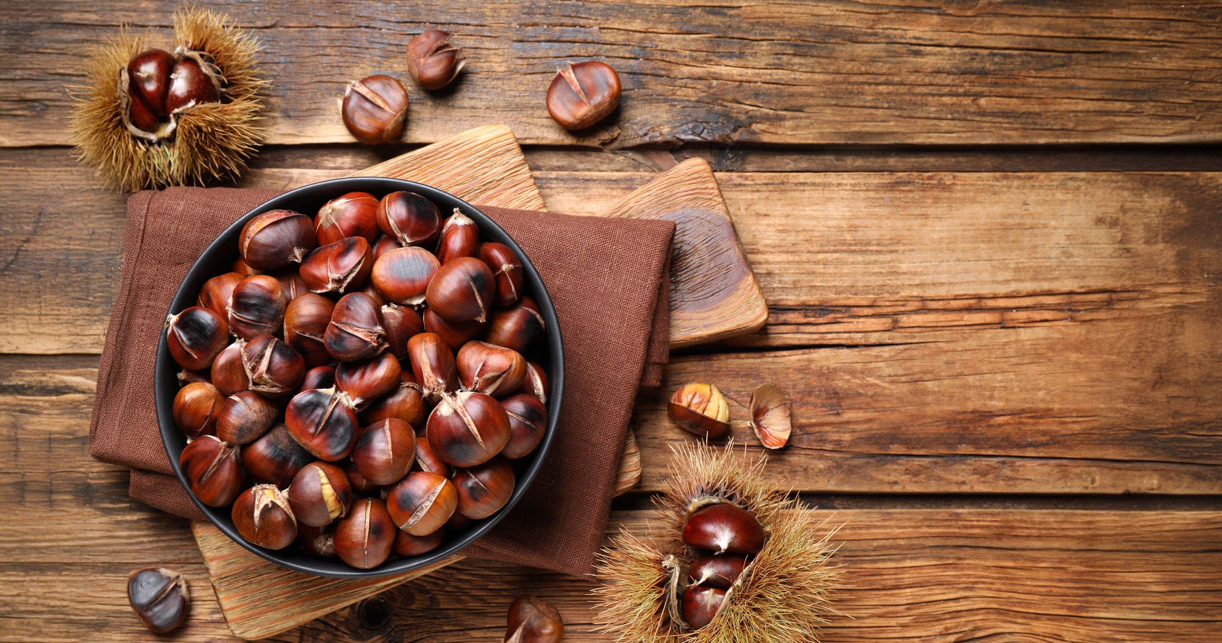Superfood Esskastanien Holztisch mit einer Pfannen voller Esskastanien