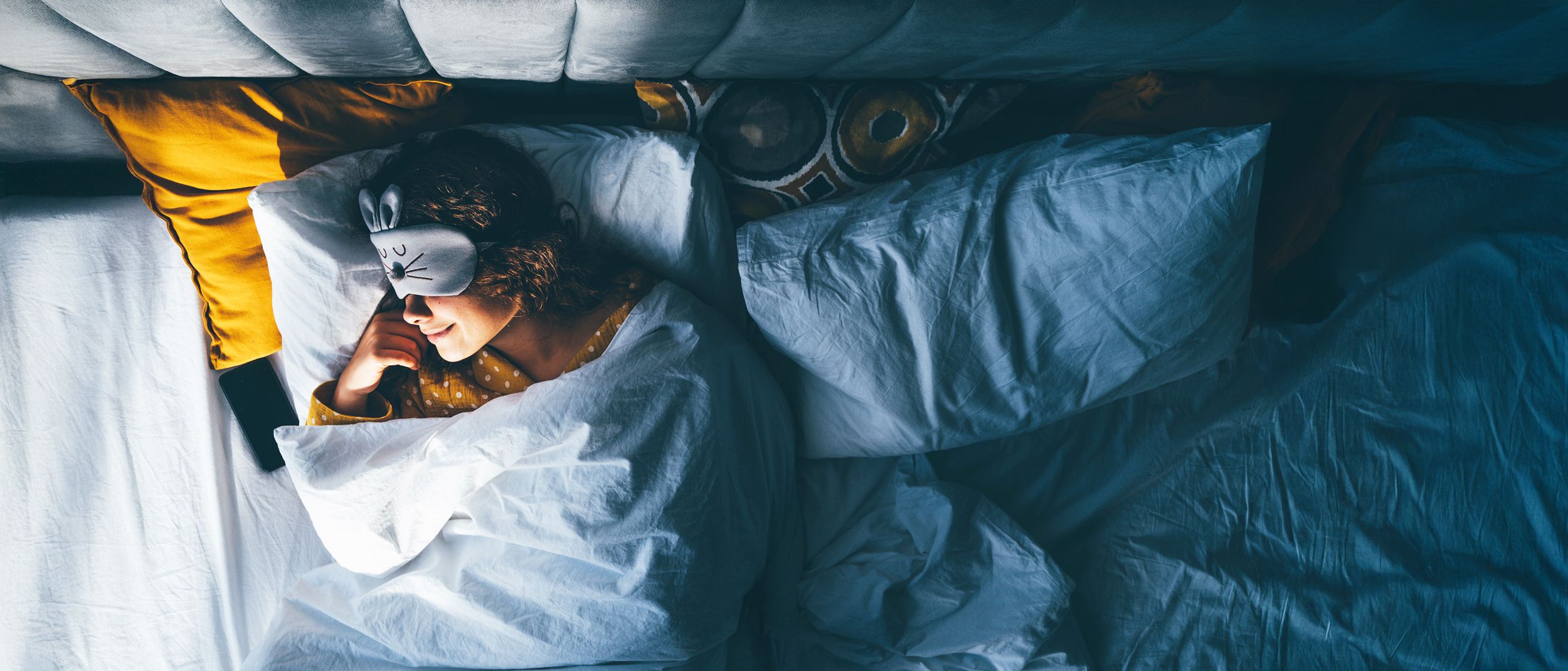 Frau liegt mit einer Augenschlafmaske im Bett und schläft