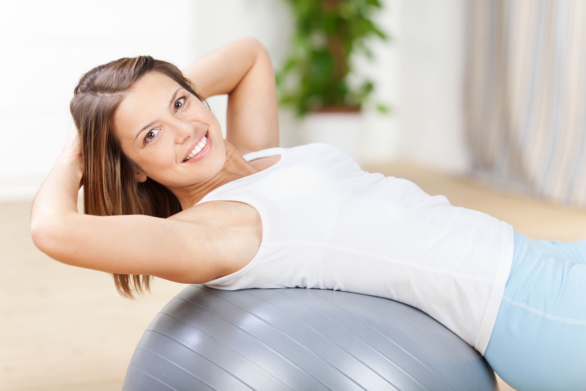 Eine Frau macht eine sportliche Übung mit einem großen, grauen Gymnastikball für mehr Rückengesundheit