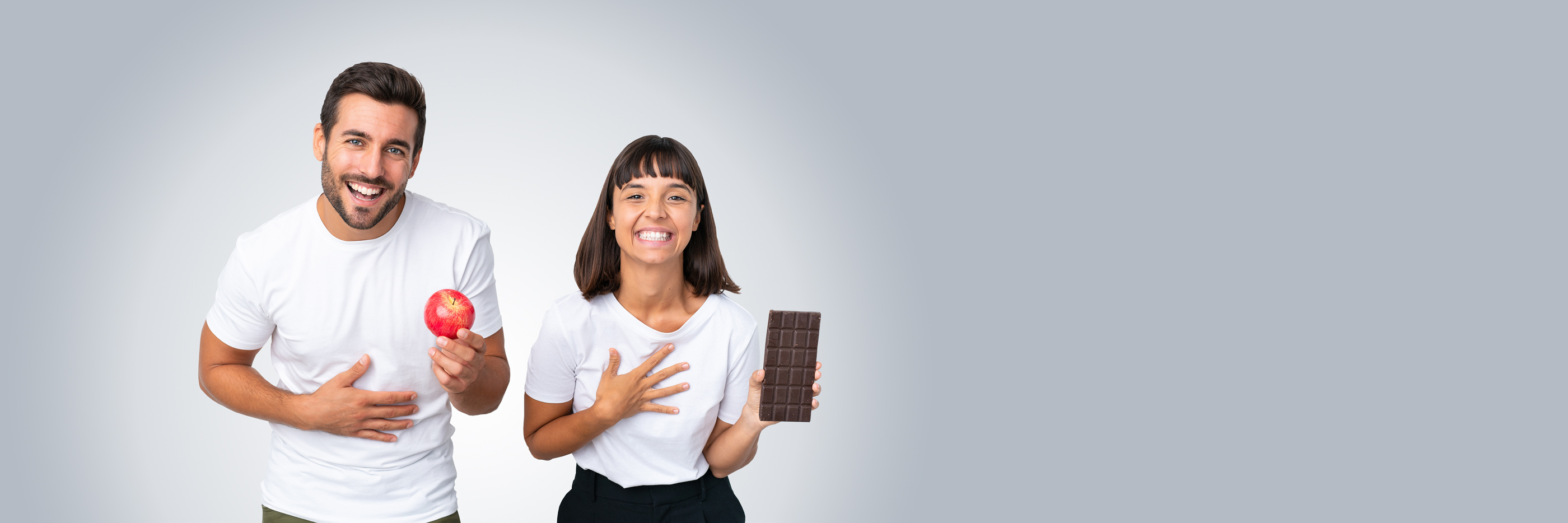 Mann hält lachend einen roten Apfel in der Hand und die Frau hält eine Tafel Schokolade