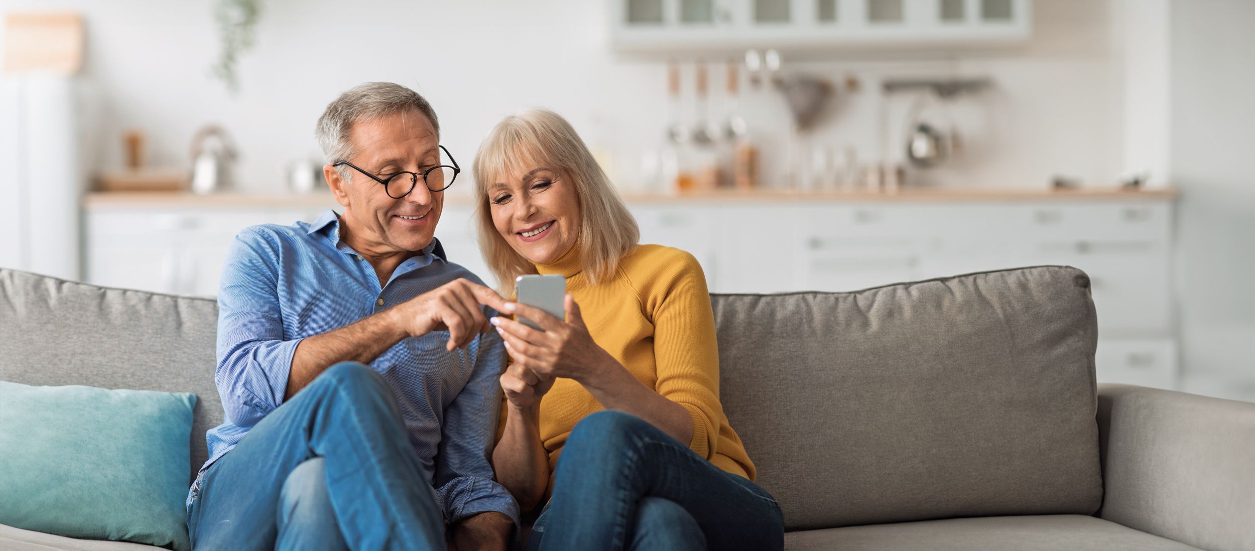Älteres Paar sitzt auf einer Couch und nutzt gemeinsam ein Smartphone