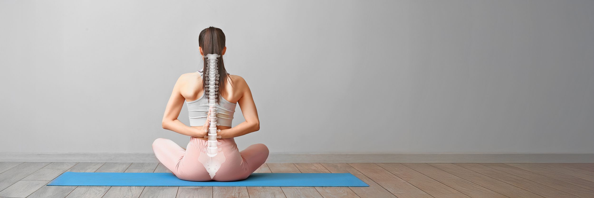 Frau in Sportkleidung sitzt auf eine Yogamatte und zeigt ihre Wirbelsäule