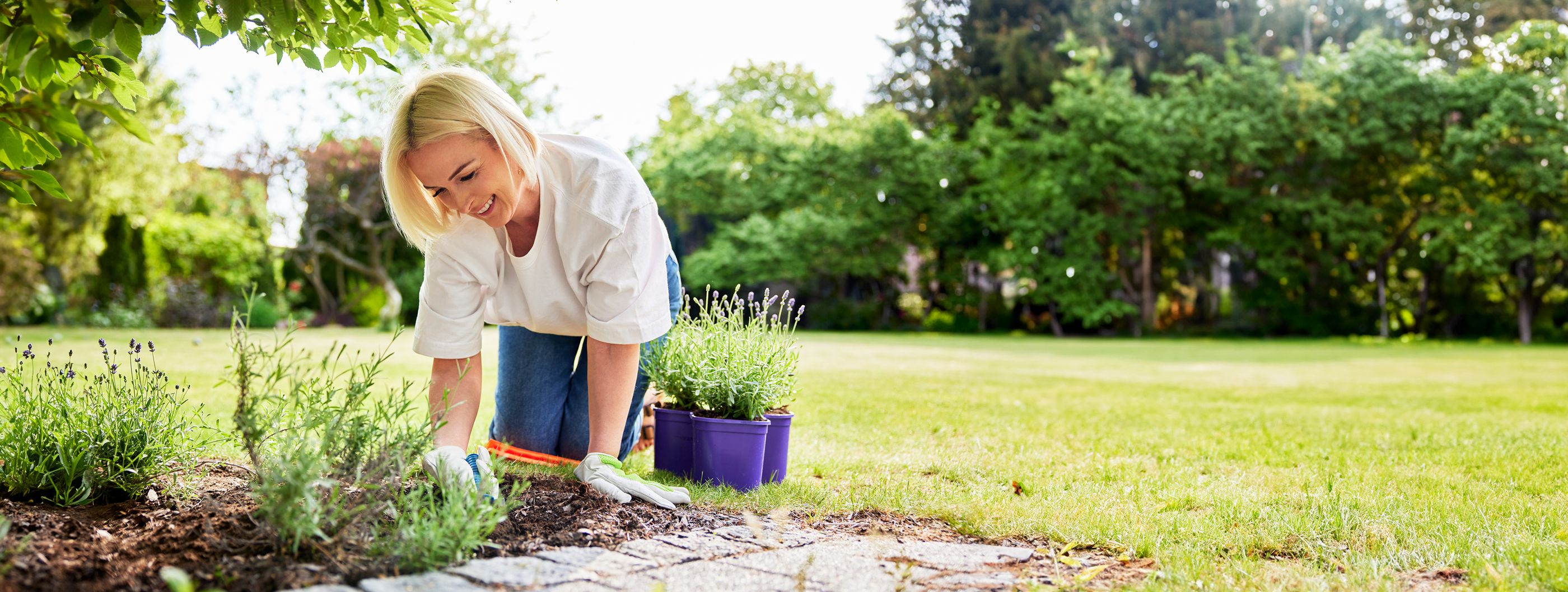 Gesunde Gartenarbeit Frau kniet vor einem Beet auf dem rasen und verrichtet mit Freude Gartenarbeit