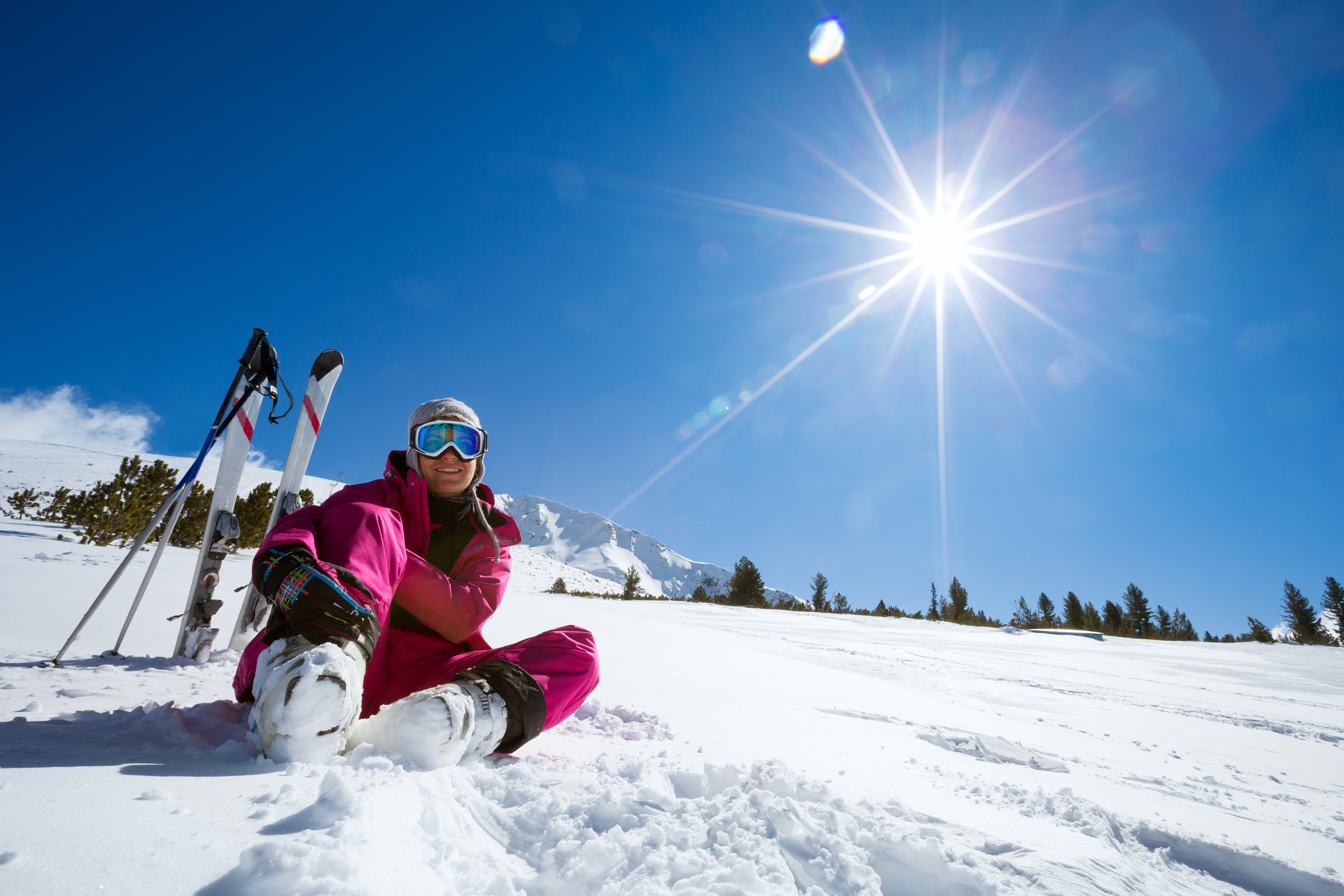 Frau sitzt im Schnee und im Hintergrund sind Ski und Skistöcke zu sehen