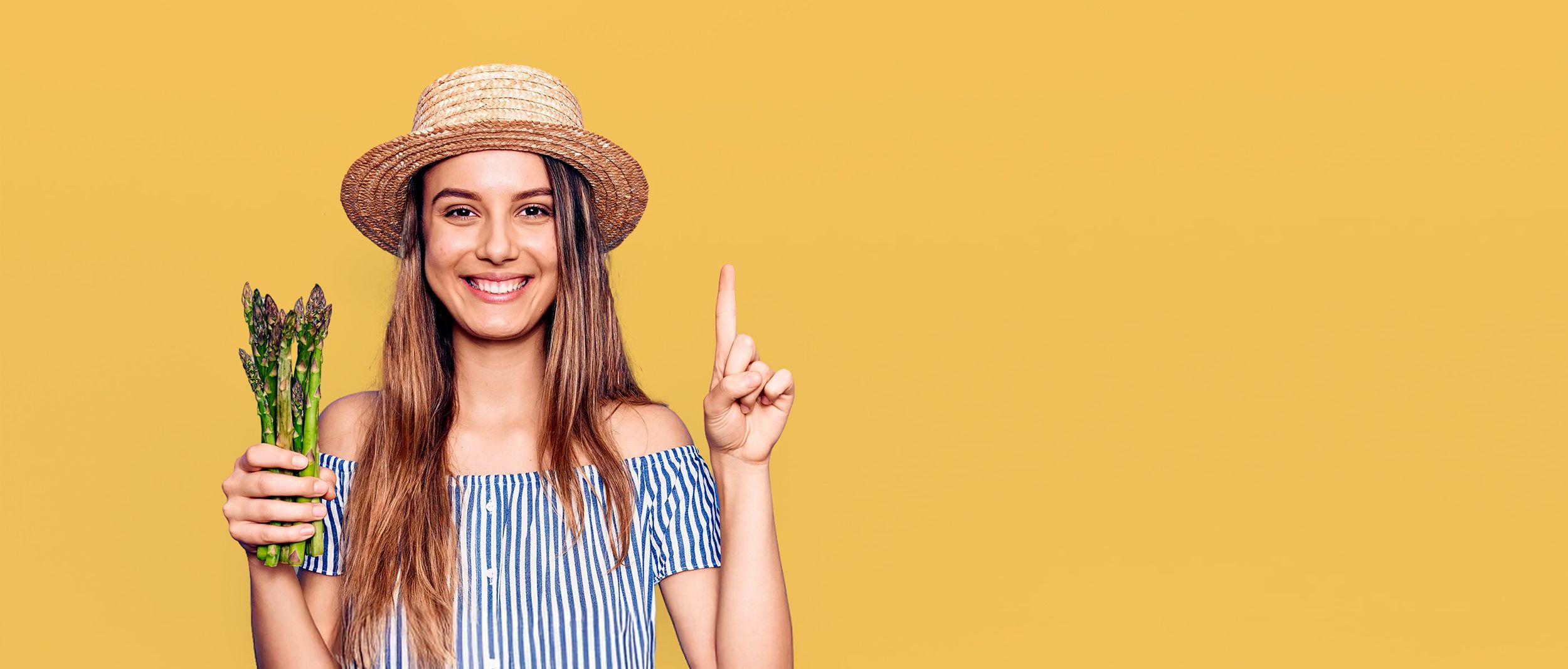 Frau mit Strohhut hält grünen Spargel in der Hand